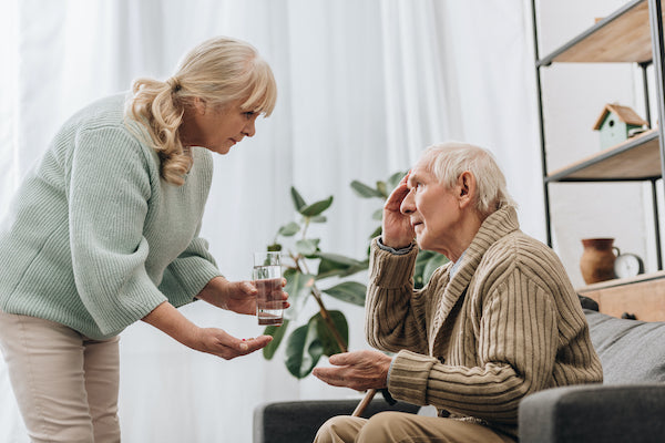 A woman is bending over and offering to help a man with dementia with his dementia medication 